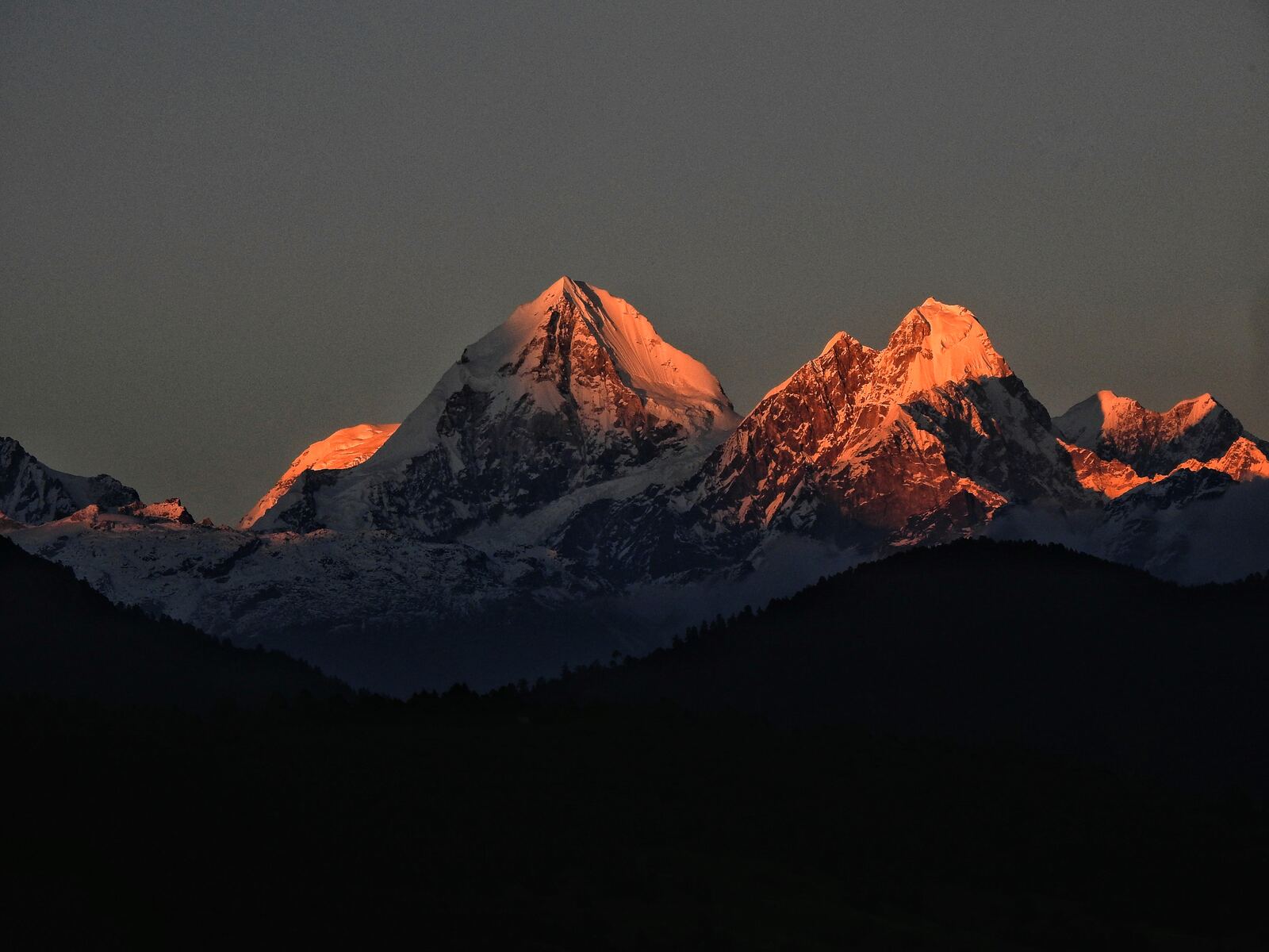 Wide shot: Langtang Lirung above the yak pastures and stone walls of Kyanjin Gompa in clear morning light