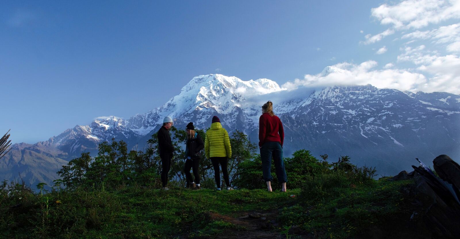 Hikers in bright jackets on a ridge below snow peaks